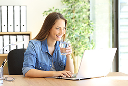  woman working on laptop and drinking a glass of water