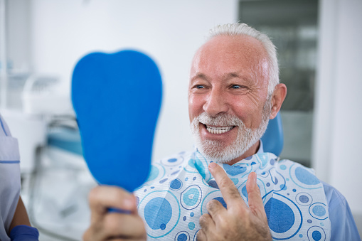 Old patient smiling in hand held mirror at The Center for Esthetic Dentistry in Grants Pass, OR