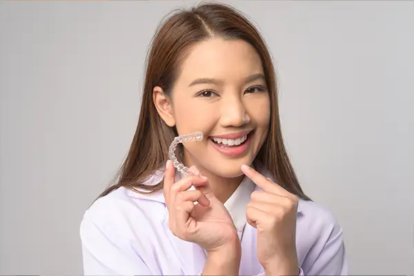 Teen girl holding and pointing to a pair of Invisalign clear aligners